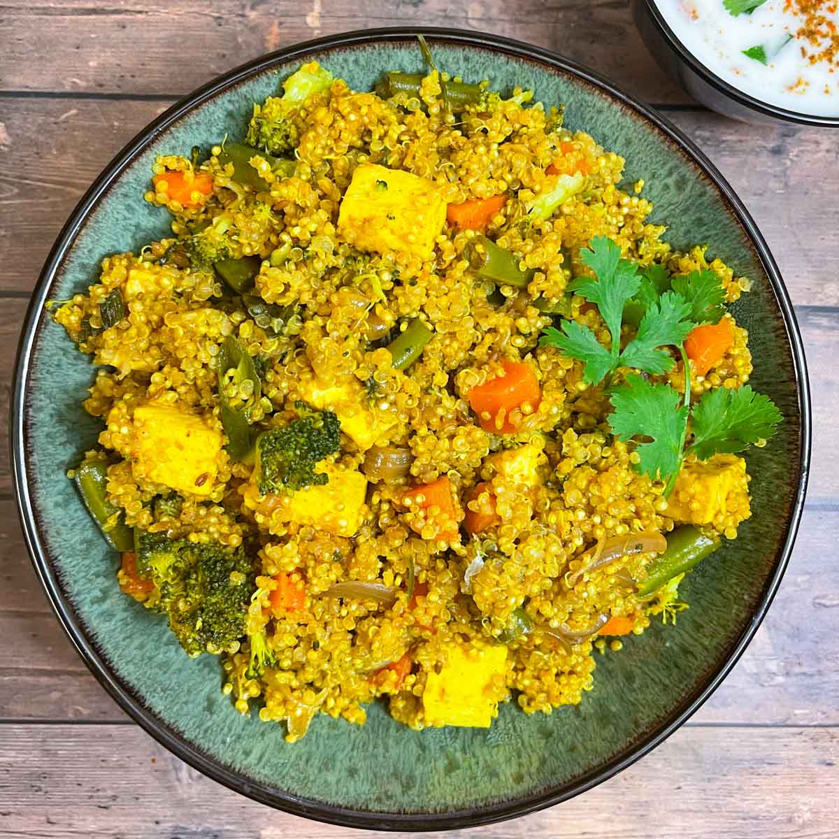 vegetable quinoa biryani served in a bowl garnished with cilantro and served with side of raita