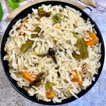 vegetable pulao served in a bowl with bay leaf on side