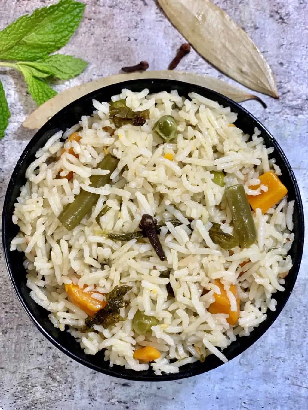 vegetable pulao served in a bowl with whole spices on the side