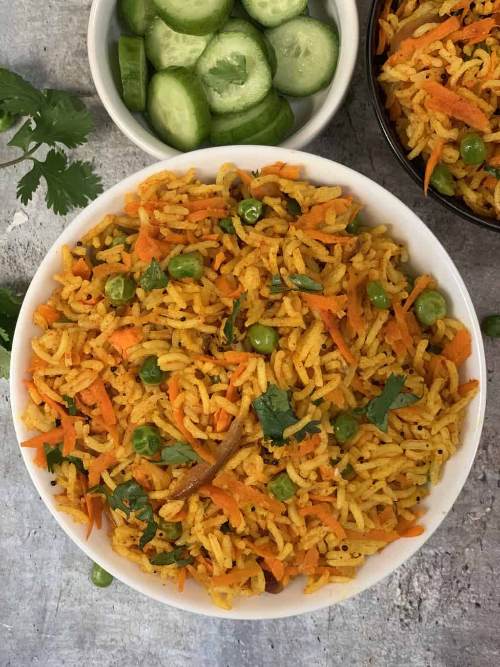 carrot rice pilaf served in a bowl garnished with cilantro with cut cucumbers on the side