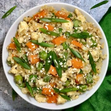 Cauliflower Fried Rice served in a white bowl garnished with sesame seeds and green onions