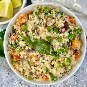 Cauliflower Upma served in a bowl with lemon wedges on the side