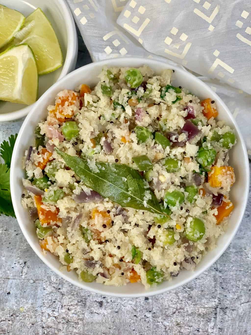 cauliflower upma served in a bowl with lemon wedges on the side