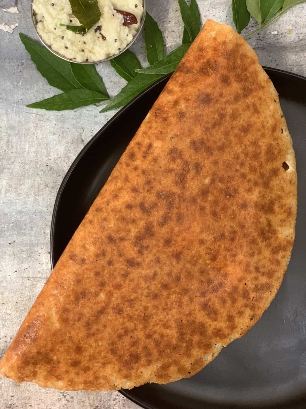 keto almond flour dosa served in a black plate with coconut chutney on the side