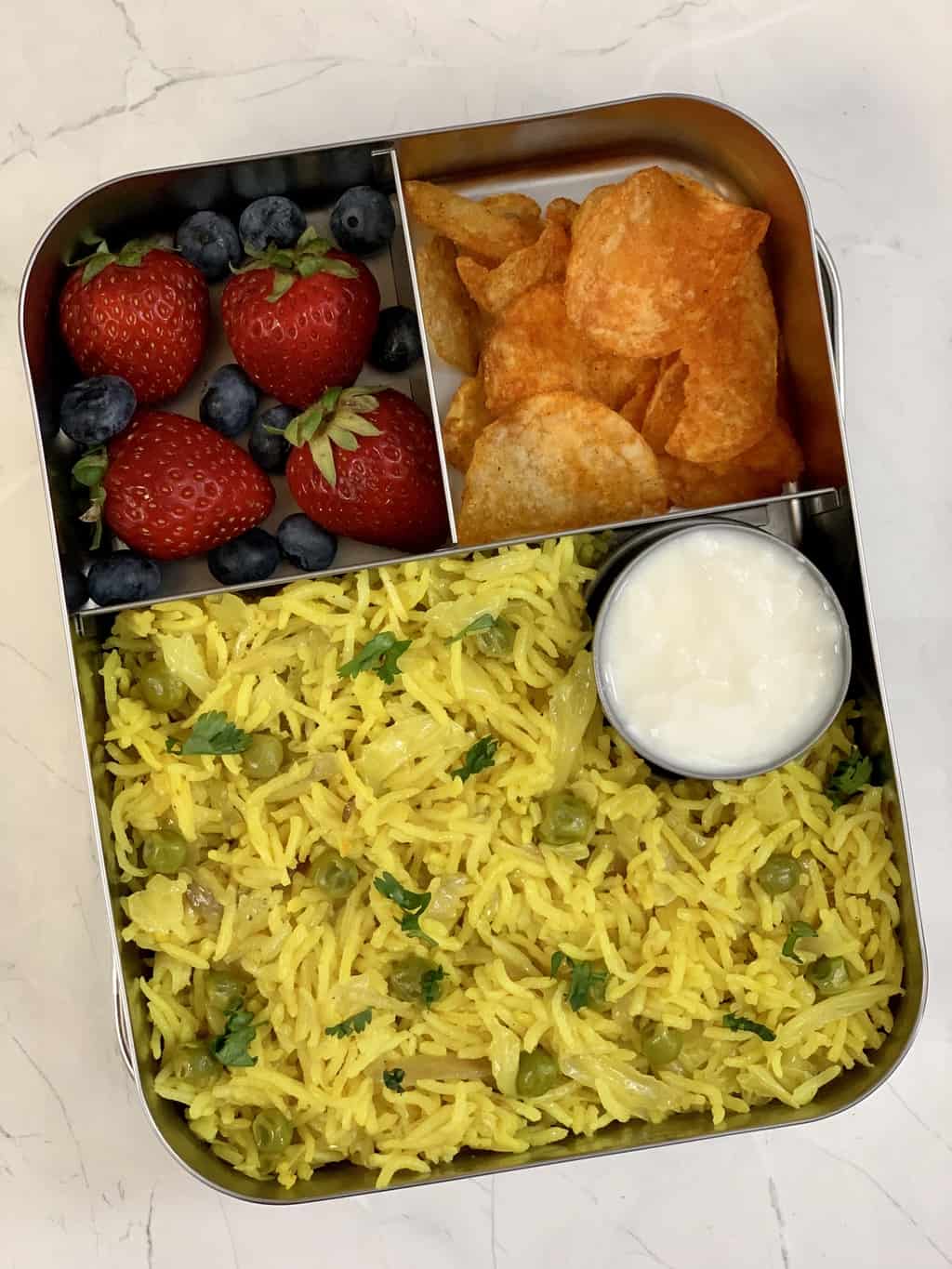 Cabbage Pulao, Yogurt, Potato Chips, Strawberries and Blueberries in steel lunch box.