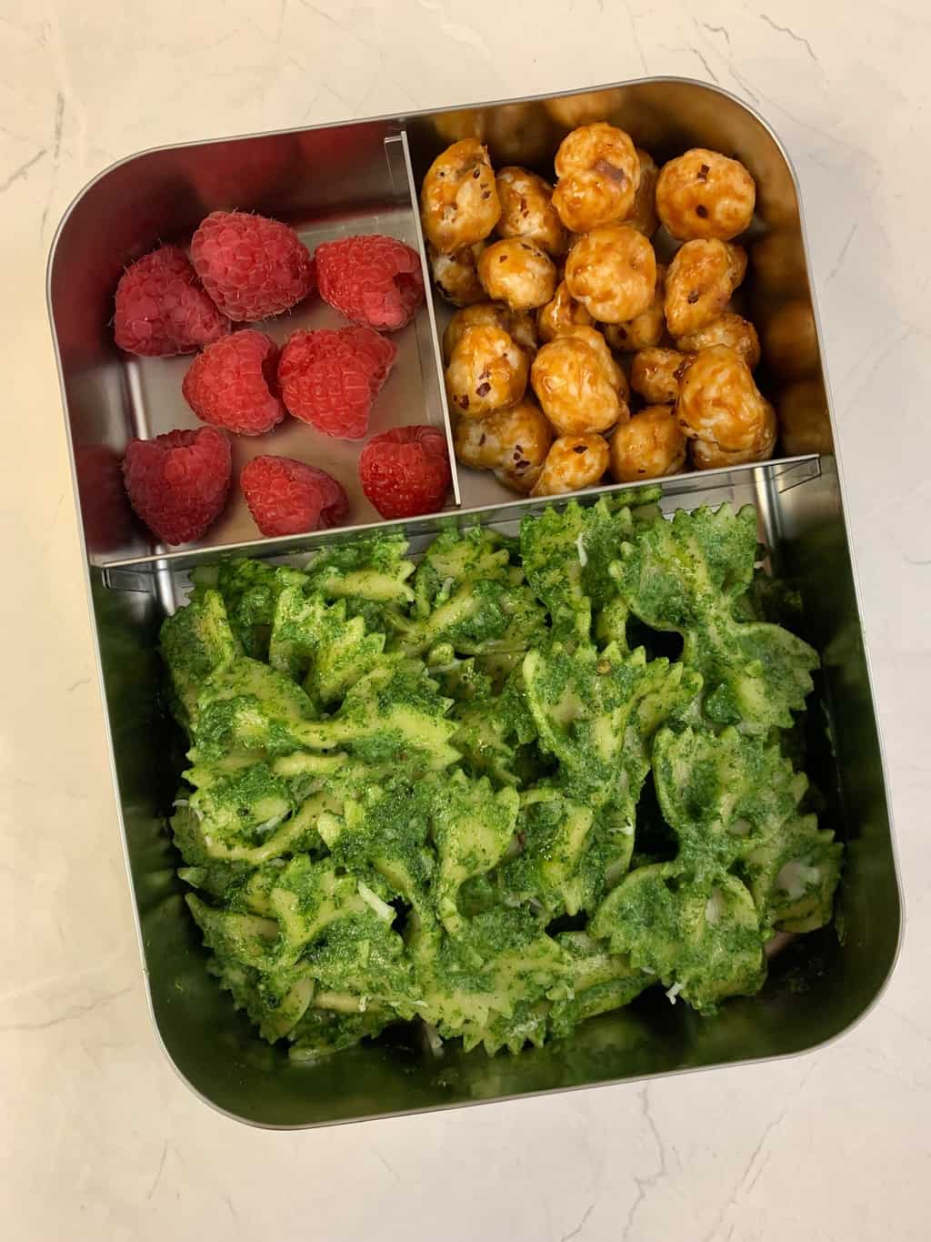 Creamy Spinach Pasta, Caramel Makhana, 
 and Raspberries in steel bento lunch box.