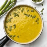 instant pot asparagus soup served in a soup bowl garnished with pumpkin seeds and asparagus and pumpkin seeds on the side