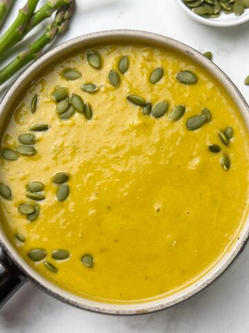 instant pot asparagus soup served in a soup bowl garnished with pumpkin seeds and asparagus and pumpkin seeds on the side