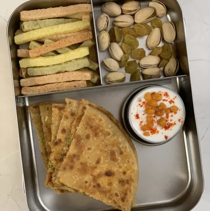 broccoli paneer paratha served in a kids lunch box with raita nuts and veggie straws on the side