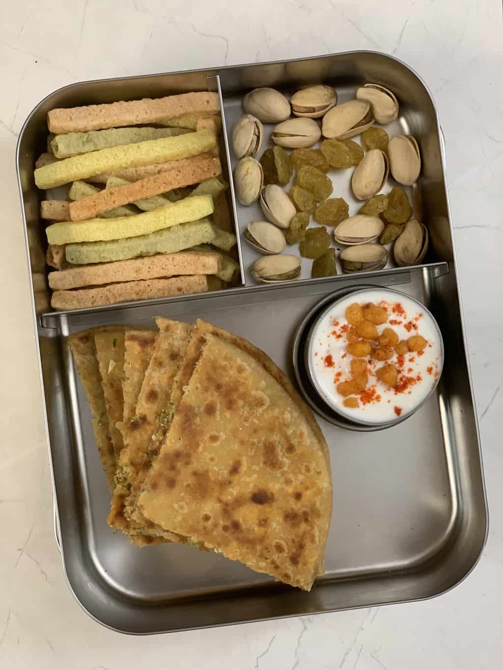 broccoli paneer paratha served in a kids lunch box with raita nuts and veggie straws on the side