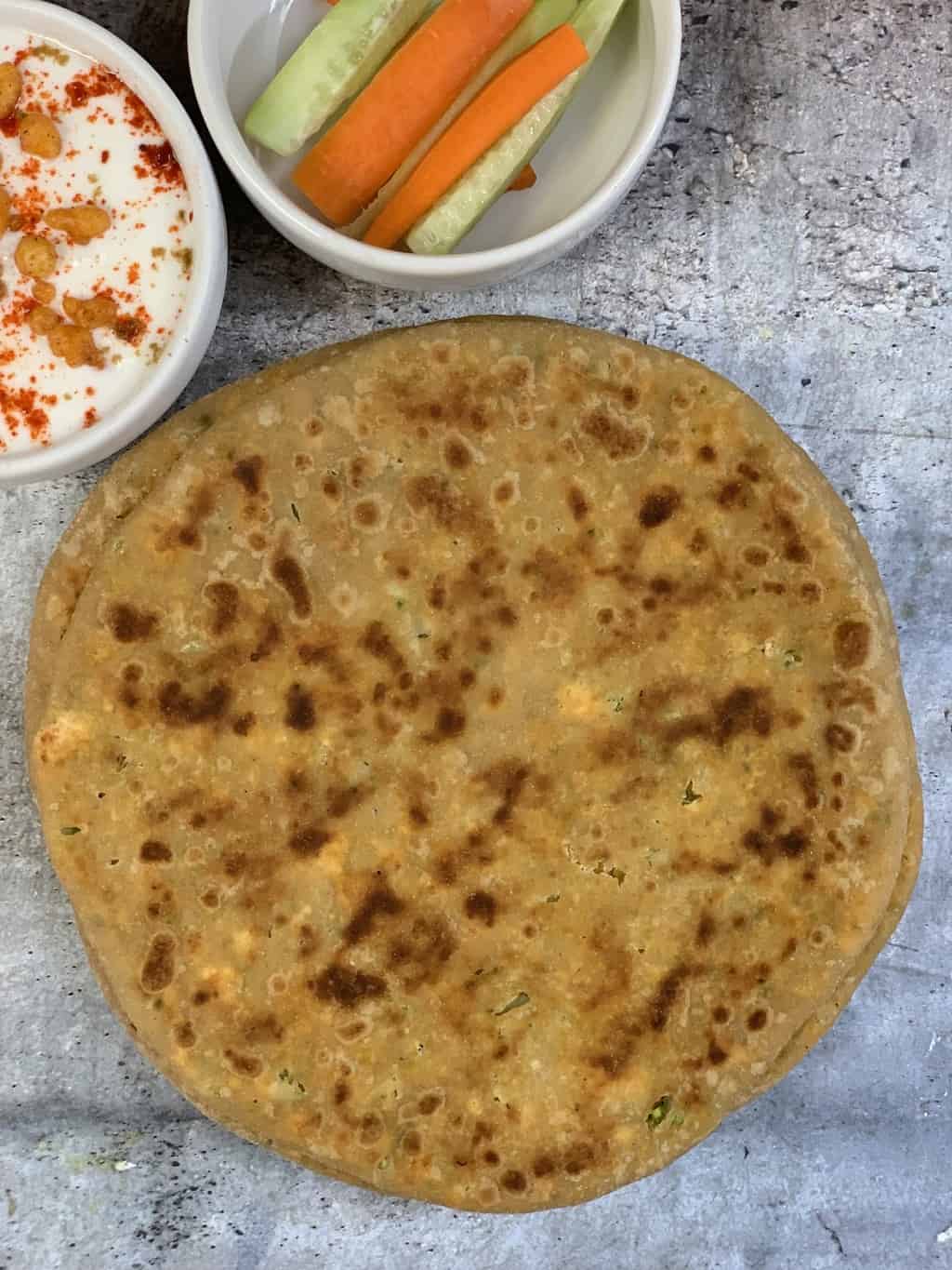 stuffed broccoli paneer paratha on a plate with cucumbers and raita on the side