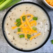 Cauliflower Soup served in a bowl garnished with green onions and shredded cheddar cheese