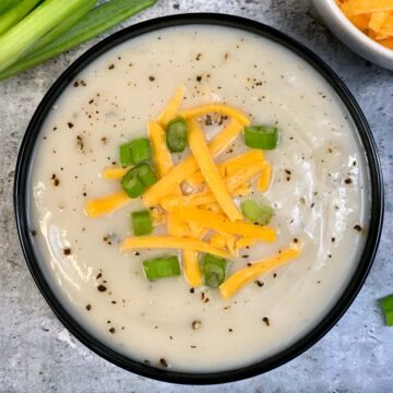 Cauliflower Soup served in a bowl garnished with green onions and shredded cheddar cheese