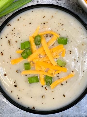 Cauliflower Soup served in a bowl garnished with green onions and shredded cheddar cheese