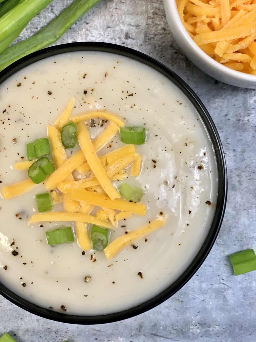 cauliflower soup served in a soup bowl garnished with cheddar cheese and green onions 