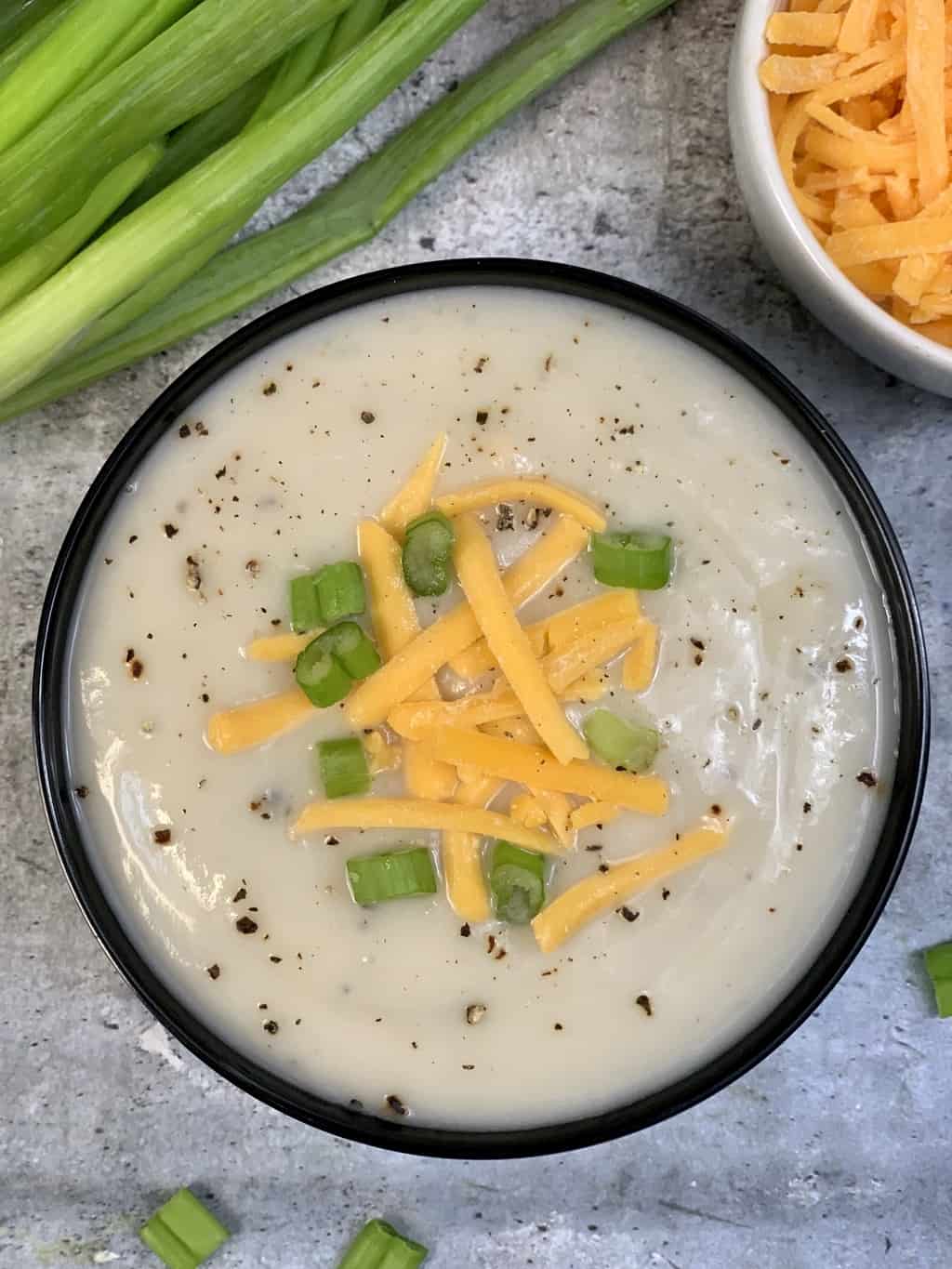 cauliflower soup keto served in a bowl with green onions and cheddar cheese on top 