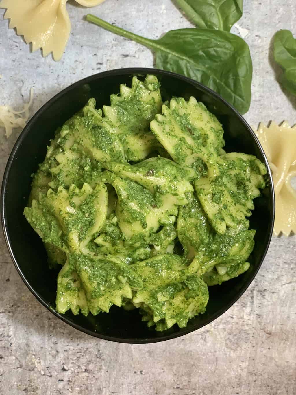 Spinach Pasta served in a black bowl with baby spinach and pasta on side