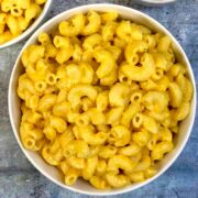 mac and cheese served in a white bowl with shredded cheddar cheese on side