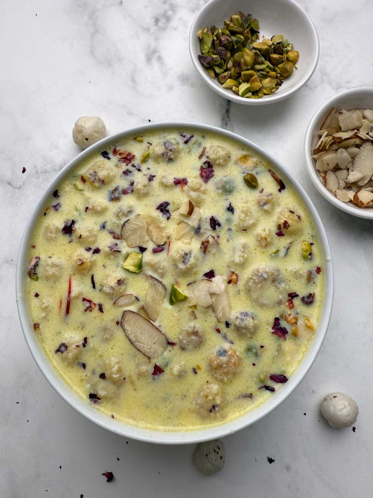 A white bowl full of phool makhana kheeer with dry fruits and nuts on the side in small bowls.