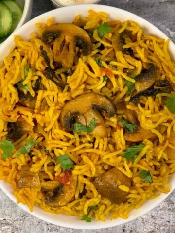 Mushroom Biryani served in a bowl with side of cucumbers