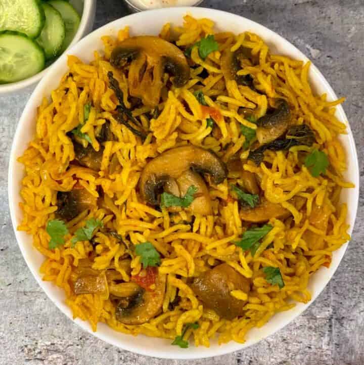 Mushroom Biryani served in a bowl with side of cucumbers
