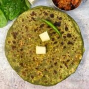 palak paneer paratha served on a plate topped with butter and with a side of pickle