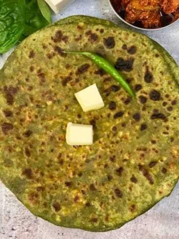 palak paneer paratha served on a plate topped with butter and with a side of pickle