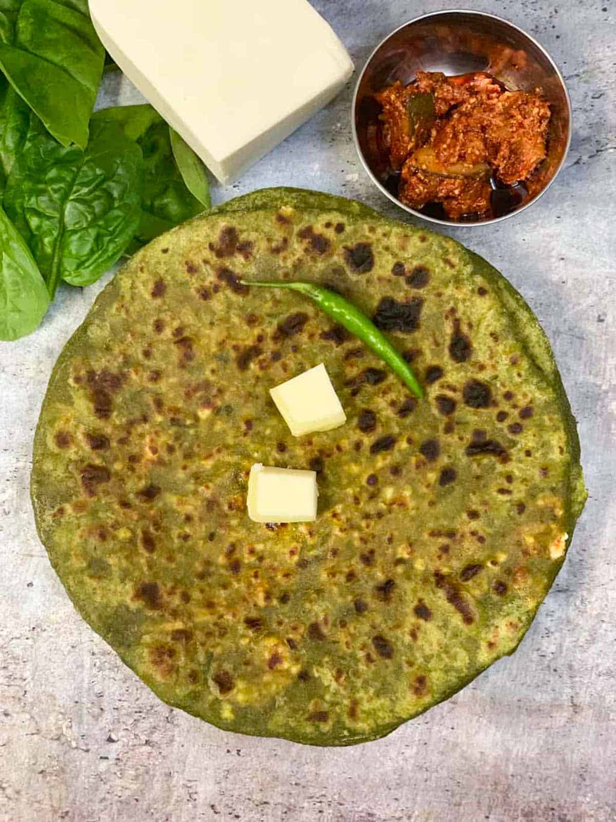 palak paneer paratha served on a plate topped with butter and with a side of pickle