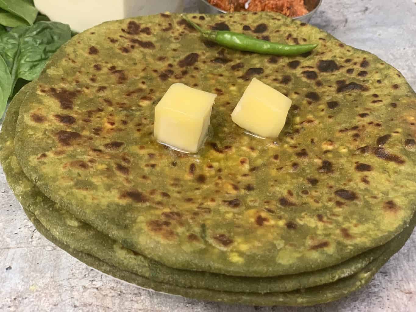 palak paneer paratha topped with butter served on a plate