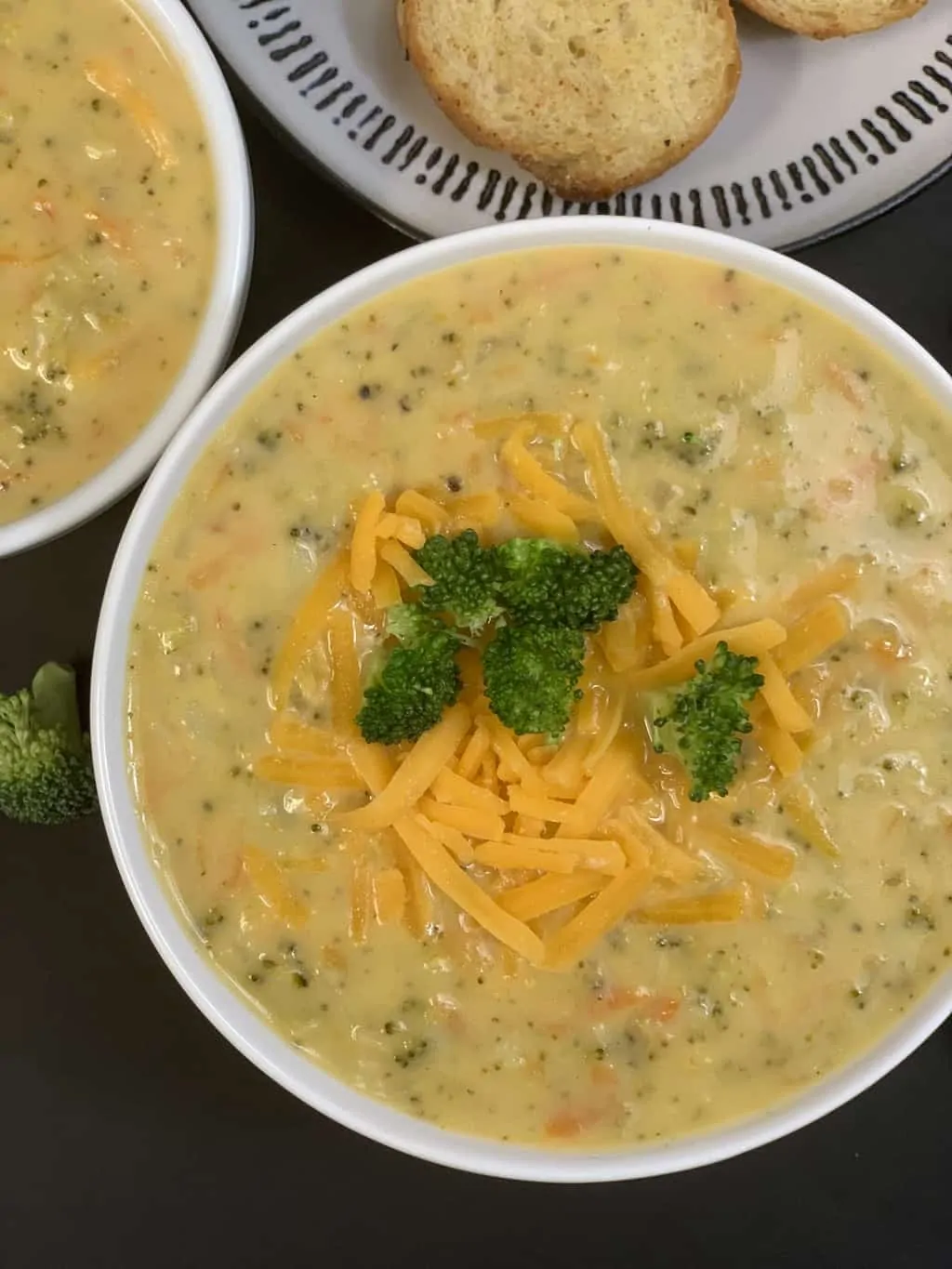 broccoli cheese soup served in a bowl garnished with cheddar cheese and cooked broccoli on top and crusty bread on the side