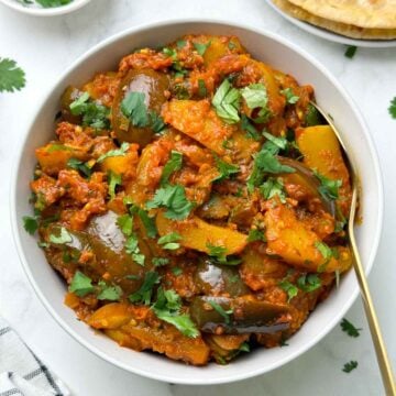 aloo baigan served in a bowl with a spoon with roti and coriander leaves on the side