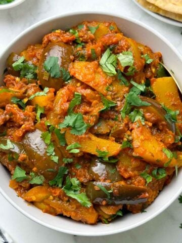 aloo baigan served in a bowl with a spoon with roti and coriander leaves on the side