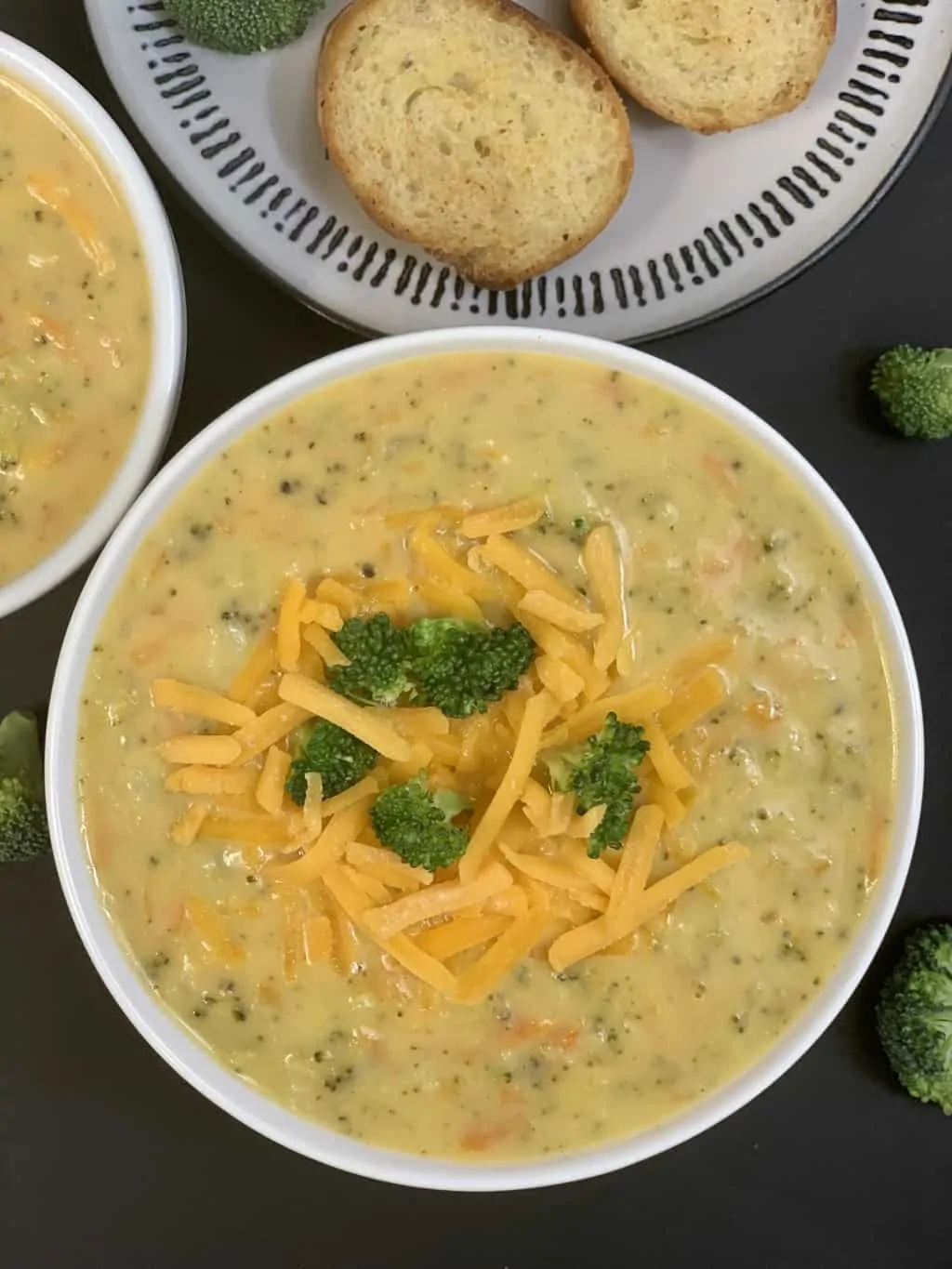 broccoli cheddar soup served in a bowl garnished with sharp cheddar cheese and cooked broccoli with garlic bread on the side