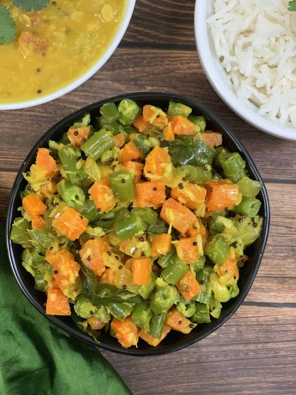 carrot beans poriyal served in a bowl with side of steamed rice and dal