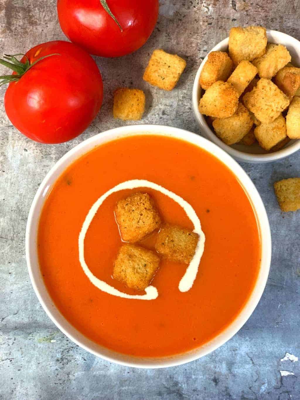 instant pot tomato soup served in a bowl topped with cream and bread croutons and tomato and bread croutons on the side