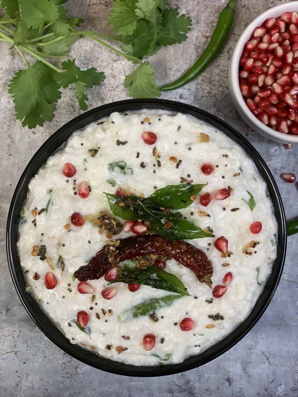 curd rice served in a bowl topped with tempering and in the side pomegranate arils in a bowl