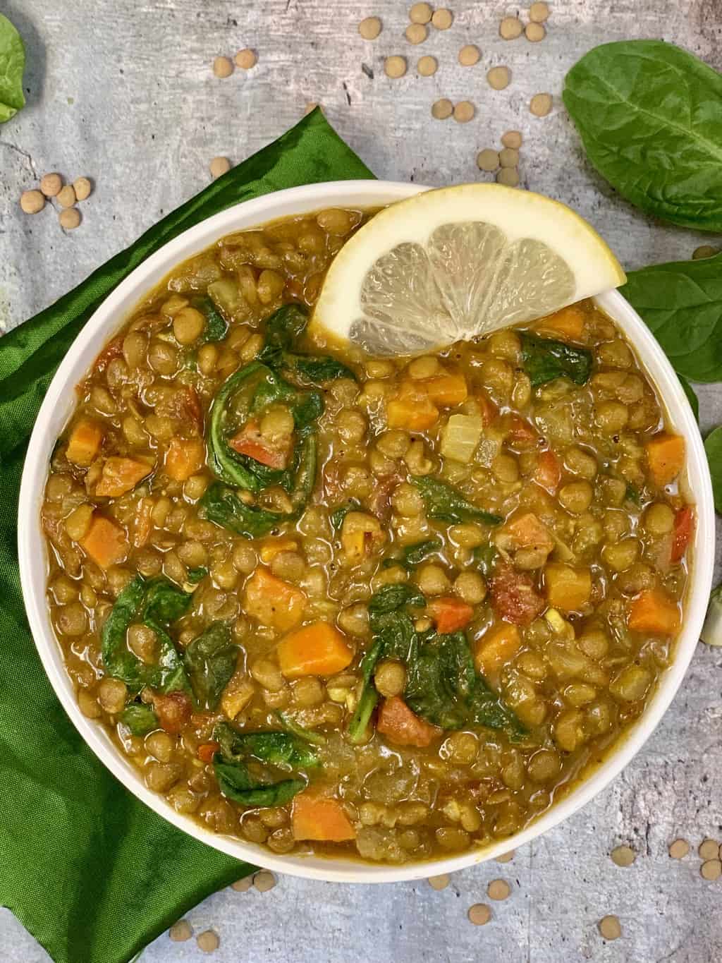 instant pot green lentil soup with coconut milk served in a white bowl with lemon wedge on top and spinach on side