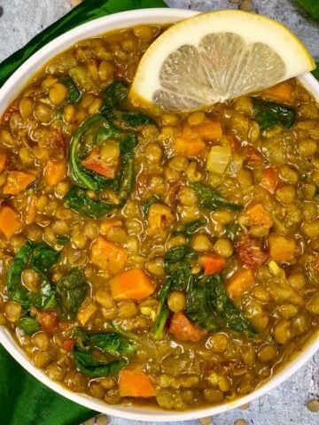 green lentil soup served in a bowl with lemon wedge on top