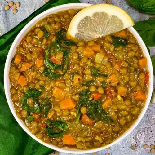 green lentil soup served in a bowl with lemon wedge on top