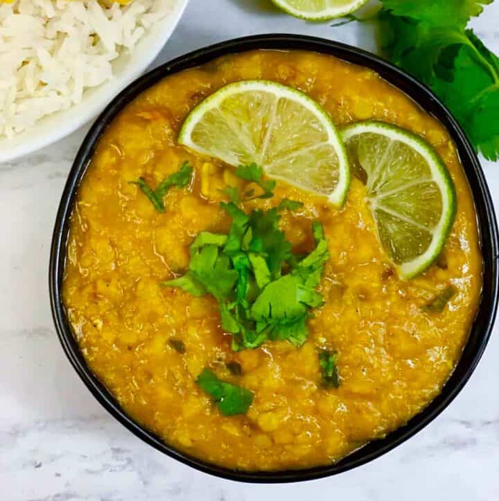 Masoor dal served in a bowl with cilantro and lemon wedge on the top and with a side of rice