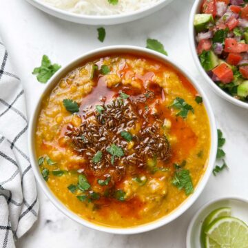 masoor dal(red lentil dal) served in a bowl with tempering on the top with side of salad and lime wedges