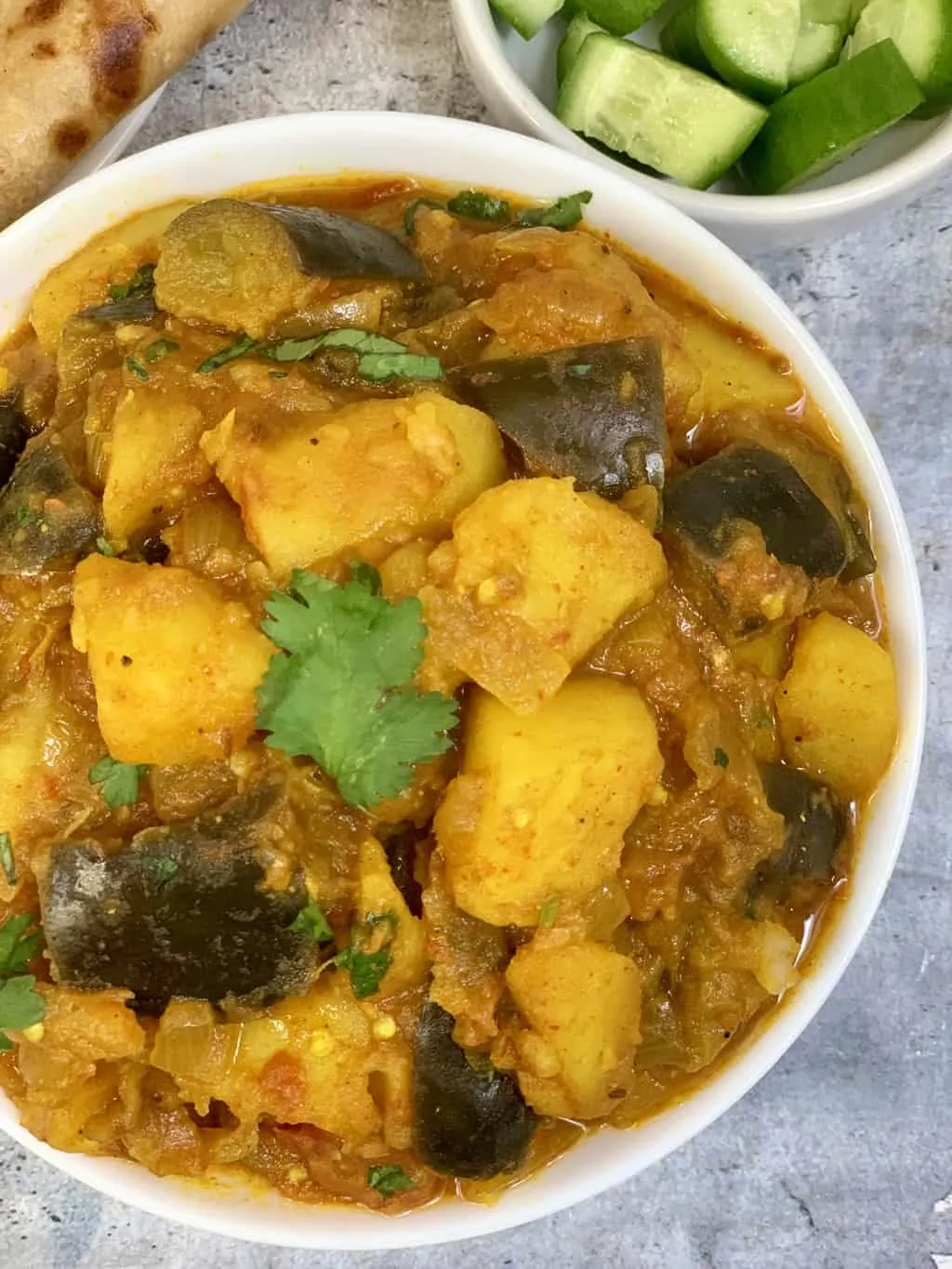 aloo baingan served in abowl with cucumber on the side