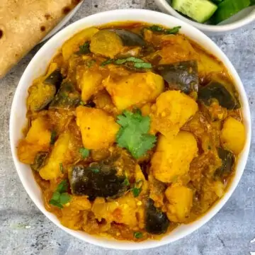 Aloo Baingan Masala served in a bowl with side of chapati and sliced cucumbers