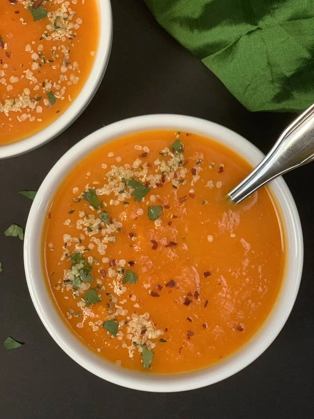 carrot soup served in a bowl garnished with hemp seeds chili flakes and cilantro