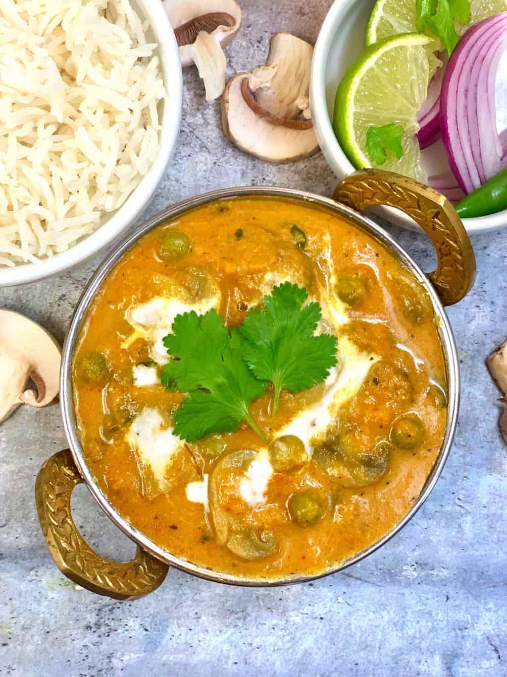 mushroom curry served in a kadai topped with cream and cilantro with a side of rice