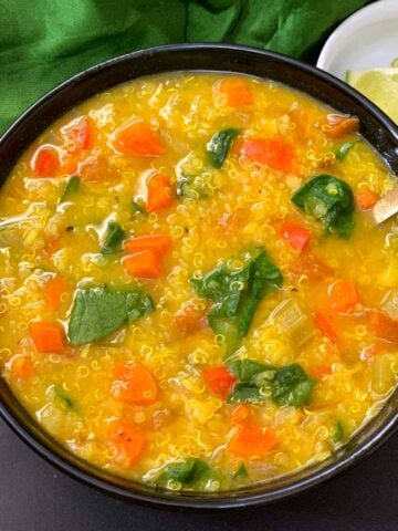 Vegetable Lentil Quinoa Soup served in a black bowl with lemon wedges on the side