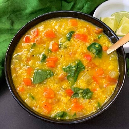 Vegetable Lentil Quinoa Soup served in a black bowl with lemon wedges on the side