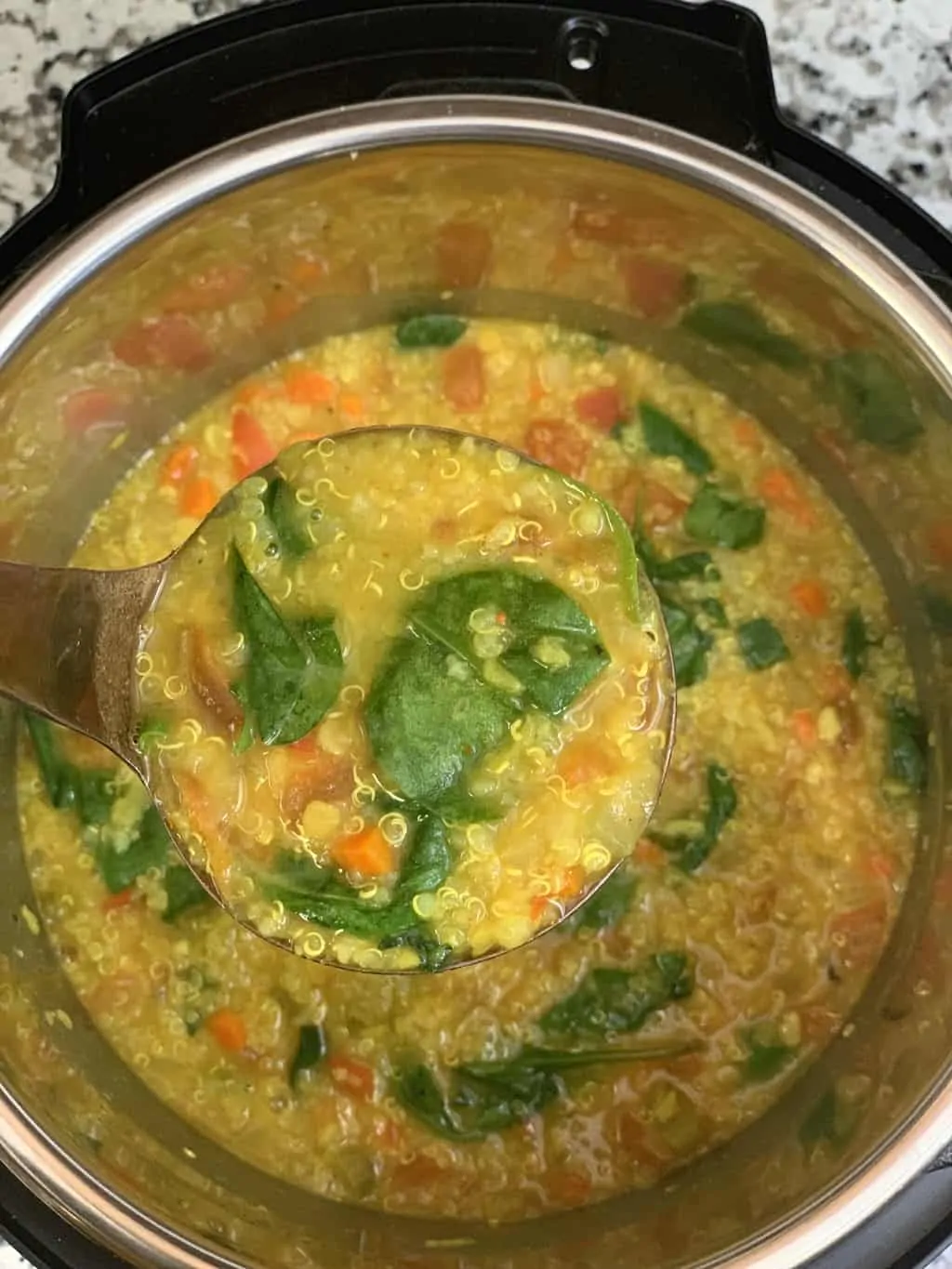 vegetable lentil quinoa soup in the instant pot insert with a spoon full of soup