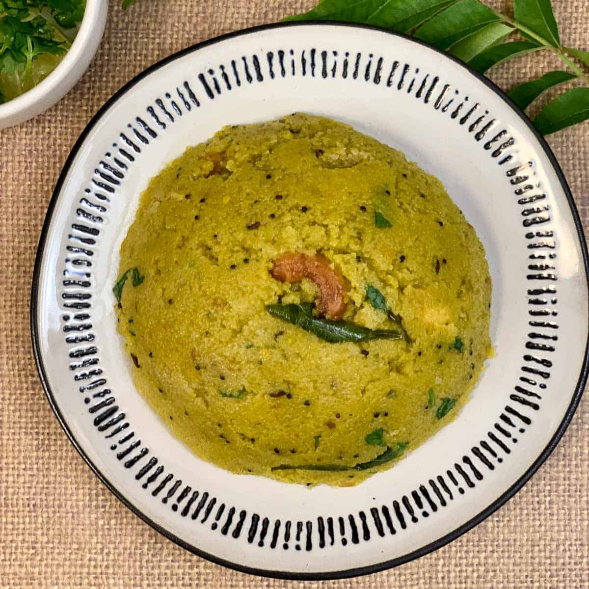 spinach rava upma served in a plate with curry leaves on side