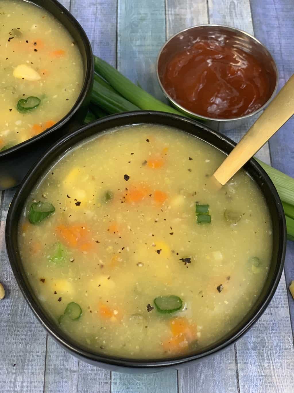 sweet corn soup served in a soup bowl with spoon and ketchup on the side